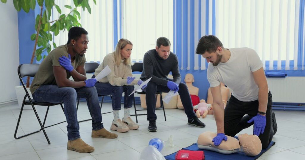 Formateur en secourisme réalisant une démonstration de compressions thoraciques sur mannequin devant un groupe en formation